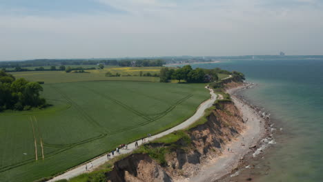 Peaceful-scenery-in-Brodten,-Germany,-aerial-drone-view-of-beach-shoreline-coast-facing-Baltic-sea-with-vast-green-spring-field,-dolly-in,-day